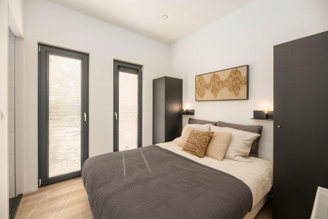 Dormitorio moderno con cama doble, armarios negros y ventanas grandes en Cannenburch, Veluwepark de Bosgraaf.