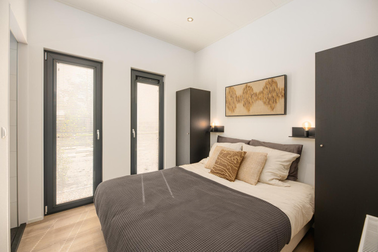 Modernes Schlafzimmer mit Doppelbett, schwarzen Schränken und großen Fenstern bei Cannenburch, Veluwepark de Bosgraaf.