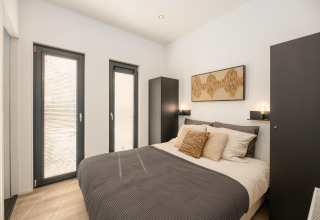 Dormitorio moderno con cama doble, armarios negros y ventanas grandes en Cannenburch, Veluwepark de Bosgraaf.