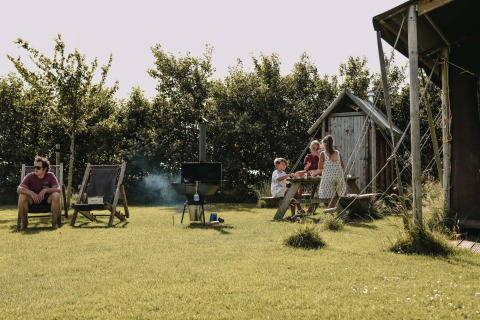Familia disfruta de picnic y relax en Feather Down Boerderij Ameland, parque vacacional en Frisia, Países Bajos.