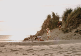 Bambini che giocano sulle dune di sabbia al parco vacanze Feather Down Boerderij Ameland in Frisia, Paesi Bassi al tramonto.