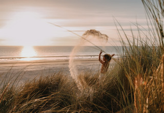 Bambino gioca tra le dune al tramonto sulla spiaggia di Feather Down Boerderij Ameland, Friesland, Paesi Bassi.