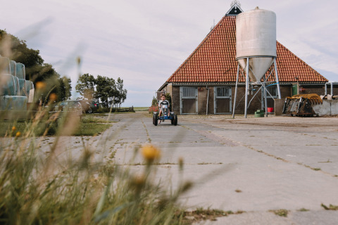 Bambino su go-kart a pedali davanti a un fienile nel parco vacanze Feather Down Boerderij Ameland in Frisia.