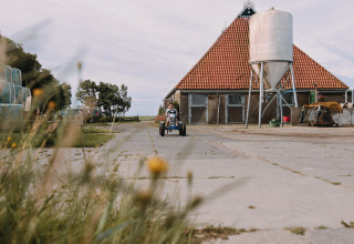 Barn kører på pedaldrevet gokart foran en lade med rødt tegltag på Feather Down Boerderij Ameland, Friesland.