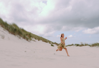 Bambina corre a piedi nudi tra le dune sabbiose vicino a Hollum, Frisia, Paesi Bassi, sotto cielo nuvoloso.