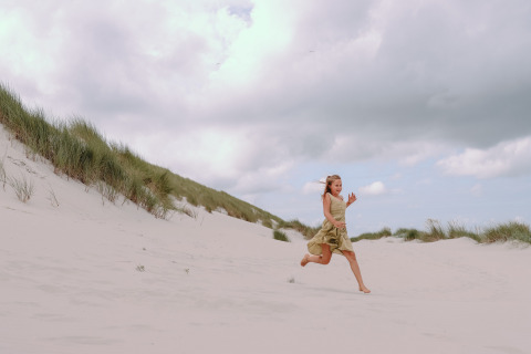 Meisje loopt blootsvoets door zandduinen vlak bij Hollum, Friesland, Nederland, onder een grijze lucht.