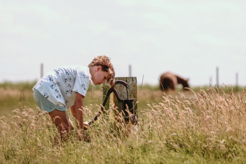 Un niño se inclina sobre una vieja bomba de agua en un campo en Feather Down Boerderij Ameland, Frisia.