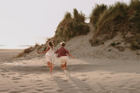 Twee kinderen rennen op een zandduin aan het strand in Feather Down Boerderij Ameland vakantiepark, Friesland, Nederland.