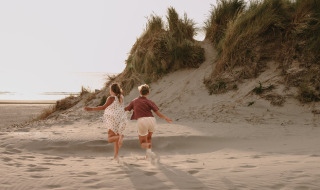 To børn løber op ad en sandklit ved stranden i Feather Down Boerderij Ameland ferielandbrug, Friesland, Holland.