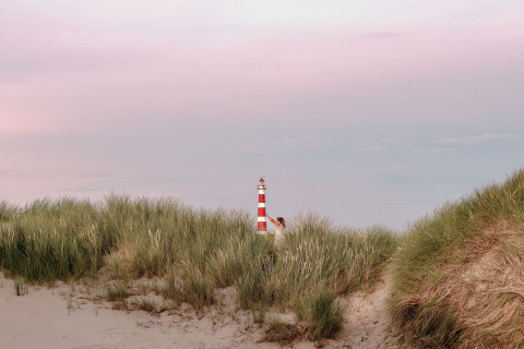 Un faro rojo y blanco se asoma entre la hierba de las dunas en Feather Down Boerderij Ameland, Frisia, Países Bajos.