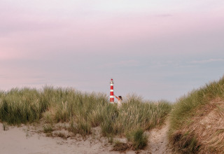 Een rood-witte vuurtoren verschijnt boven het duingras bij Feather Down Boerderij Ameland in Friesland.