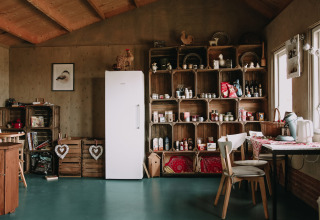 Cocina rústica con cajas de madera, nevera y comedor en Feather Down Boerderij Ameland, Friesland, Países Bajos.