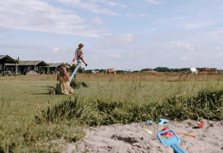 Børn leger på en vippe med udsigt til telte og heste på Feather Down Boerderij Ameland feriepark i Friesland.