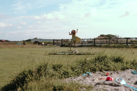 Bambina con vestito giallo che salta sull’erba al Feather Down Boerderij Ameland, Friesland, Paesi Bassi.