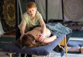 En massør giver en afslappende rygmassage til en kvinde, der ligger i en pod med dæmpet belysning.