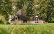 Et hyggeligt glamping-hus i en grøn skov, omgivet af træer og græs, ideelt til afslapning i naturen.
