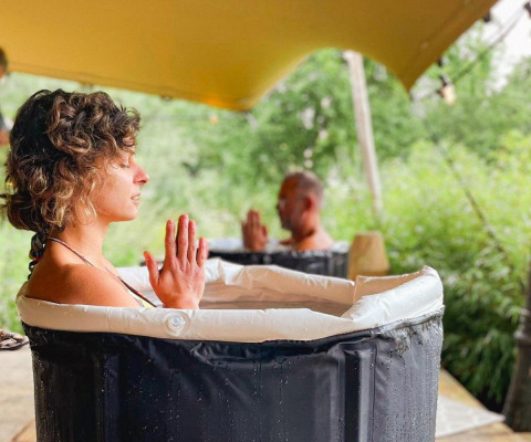 Zwei Personen sitzen meditierend in separaten Wasserbecken unter einem Pavillon, mit gefalteten Händen.