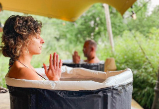 Two people sit in individual water tubs under a canopy pod, meditating with hands pressed together.