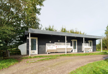 Edificio de baños moderno en un glamping, con lavabos exteriores y rodeado de vegetación verde.