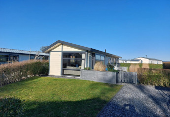 Cabaña Velthorst en EuroParcs Parc du Soleil, Países Bajos, césped verde, setos y cielo azul despejado.