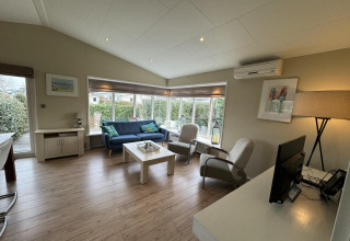 Luminoso salón moderno de una cabaña Velthorst en EuroParcs Parc du Soleil, con sofá, sillones y grandes ventanales.