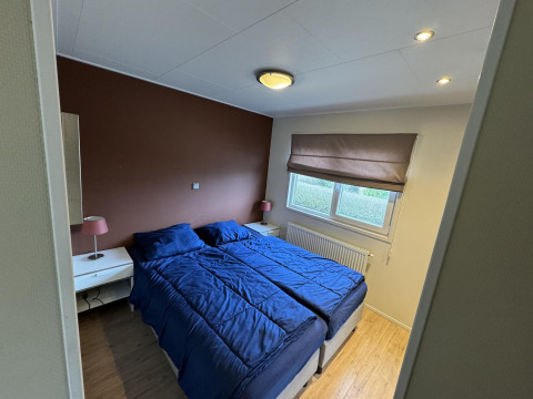 Dormitorio en la cabaña Velthorst en EuroParcs Parc du Soleil, Países Bajos, con ropa de cama azul y pared marrón.