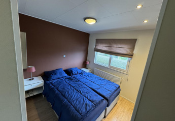 Dormitorio en la cabaña Velthorst en EuroParcs Parc du Soleil, Países Bajos, con ropa de cama azul y pared marrón.