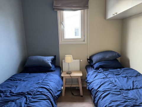 Zweibettzimmer in einer Velthorst-Hütte bei EuroParcs Parc du Soleil, mit blauer Bettwäsche und Fenster.
