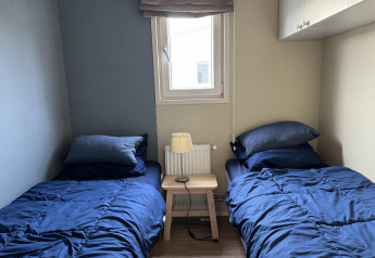 Dormitorio de la cabaña Velthorst en EuroParcs Parc du Soleil con dos camas, ropa azul y una ventana.