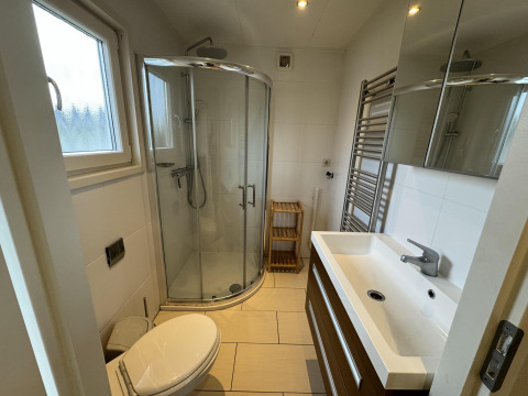 Baño moderno con ducha curva, lavabo, espejo, toallero y ventana en una cabaña en los Países Bajos.