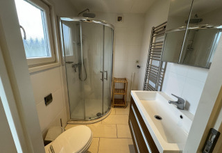 Baño moderno con ducha curva, lavabo, espejo, toallero y ventana en una cabaña en los Países Bajos.