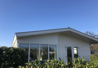 Hvid Velthorst-hytte ved EuroParcs Parc du Soleil i Holland med store vinduer og blå himmel.