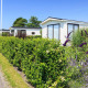 Solrig udsigt til Berkel-hytten på EuroParcs Parc du Soleil, Holland, omgivet af grønne hække og blomster.
