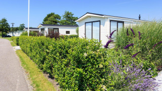 Vue ensoleillée sur le chalet Berkel à EuroParcs Parc du Soleil, Pays-Bas, entouré de haies et de fleurs.