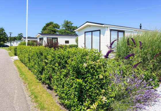 Vue ensoleillée sur le chalet Berkel à EuroParcs Parc du Soleil, Pays-Bas, entouré de haies et de fleurs.
