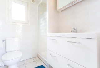 Salle de bains lumineuse avec toilettes, douche et meuble blanc dans la cabane Berkel du EuroParcs Parc du Soleil.