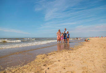 Familie geniet van een zonnige stranddag bij de Berkel-cabine, blauwe lucht en rustige zee.