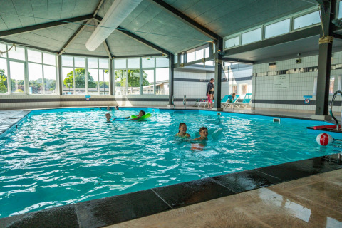 Indendørs swimmingpool ved Berkel-hytten med børn og voksne, store vinduer og liggestole ved siden.