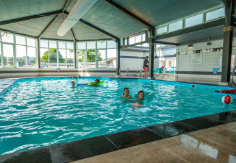 Indendørs swimmingpool ved Berkel-hytten med børn og voksne, store vinduer og liggestole ved siden.