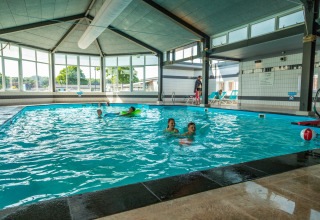 Piscina cubierta en la cabaña Berkel con niños jugando y ventanas grandes iluminando el espacio interior.