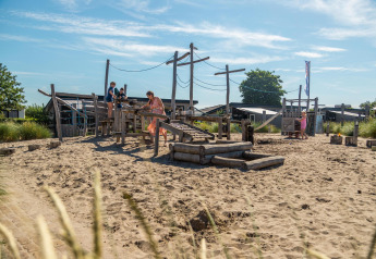 Kinderen en volwassenen spelen op een zandige speeltuin aan de Berkel-hut op een zonnige dag.