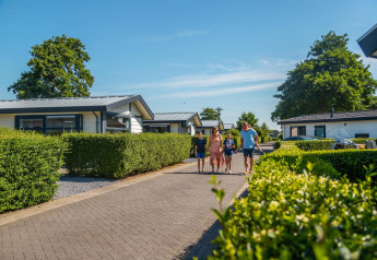 Gezin wandelt langs Berkel-huisjes in EuroParcs Parc du Soleil in Nederland op een zonnige zomerdag.