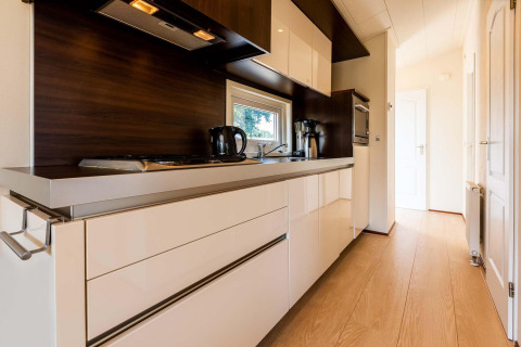 Cocina moderna con gabinetes brillantes y detalles en madera en la cabaña Berkel, EuroParcs Parc du Soleil, Países Bajos.