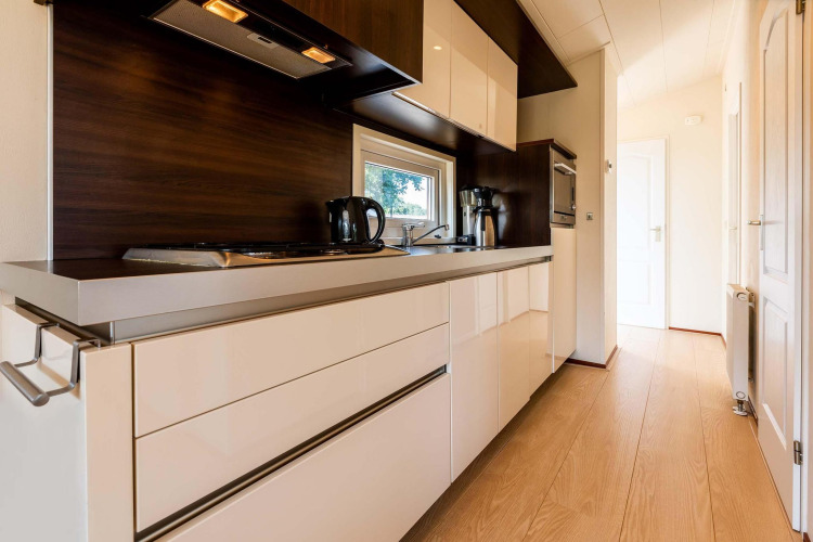 Cocina moderna con gabinetes brillantes y detalles en madera en la cabaña Berkel, EuroParcs Parc du Soleil, Países Bajos.