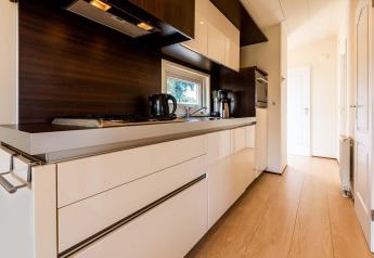 Moderne Küche mit weißen Schränken und Holzboden in der Berkel-Hütte, EuroParcs Parc du Soleil, Niederlande.