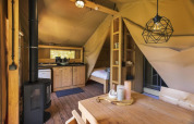 Interior de la tienda safari Comet 27 Lodges en Petite Suisse, Bélgica, con decoración de madera y cocina.