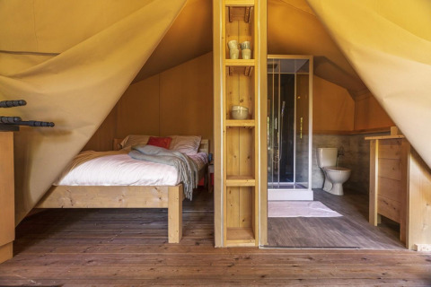 Vista interior de la tienda safari Comet 27 Lodges con cama, baño y piso de madera en Petite Suisse, Bélgica.
