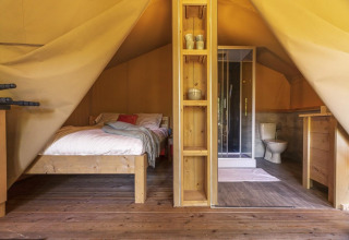 Vista interior de la tienda safari Comet 27 Lodges con cama, baño y piso de madera en Petite Suisse, Bélgica.