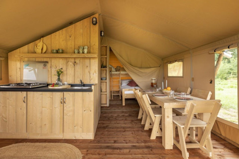 Interior de una tienda safari en Comet 27 Lodges, Petite Suisse, Bélgica, con cocina, comedor y camas.