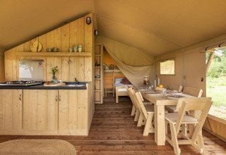Interior de una tienda safari en Comet 27 Lodges, Petite Suisse, Bélgica, con cocina, comedor y camas.